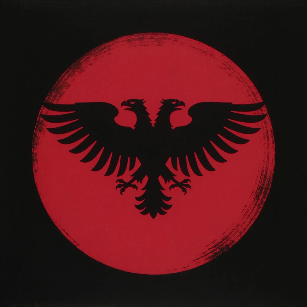 Emblème de Tomo Dhimoïla : l’aigle bicéphale albanais déployé à l’intérieur du disque rouge du soleil levant japonais